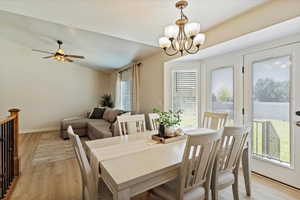 Dining space with light wood finished floors, a chandelier, lofted ceiling, and a ceiling fan
