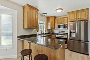 Kitchen featuring appliances with stainless steel finishes, dark stone countertops, a peninsula, a breakfast bar area, and light wood-style flooring