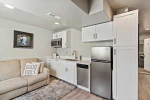 Kitchen with appliances with stainless steel finishes, light wood-style flooring, white cabinetry, open floor plan, and recessed lighting
