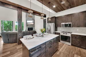 Kitchen featuring appliances with stainless steel finishes, open floor plan, wood ceiling, light wood finished floors, and a stone fireplace