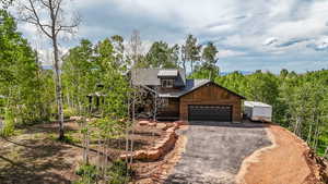 Rustic home featuring a garage, asphalt driveway, a metal roof, and a view of trees
