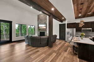 Living room with a stone fireplace, light wood-style flooring, high vaulted ceiling, a wooden ceiling with exposed beams, and recessed lighting