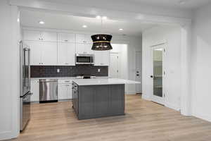 Kitchen with appliances with stainless steel finishes, light wood-style flooring, backsplash, white cabinetry, and recessed lighting