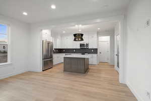 Kitchen featuring stainless steel appliances, white cabinetry, decorative backsplash, light countertops, and a kitchen island