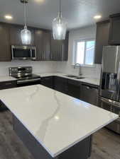 Kitchen with appliances with stainless steel finishes, dark wood-style floors, pendant lighting, light stone countertops, and recessed lighting