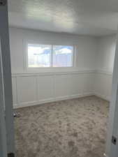 Carpeted empty room featuring a decorative wall, a textured ceiling, and wainscoting