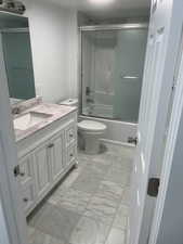 Bathroom featuring marble look tiles, vanity, and bath / shower combo with glass door