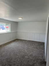 Carpeted spare room featuring a decorative wall, a textured ceiling, and a wainscoted wall