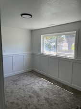 Spare room featuring a decorative wall, a textured ceiling, carpet, and a wainscoted wall