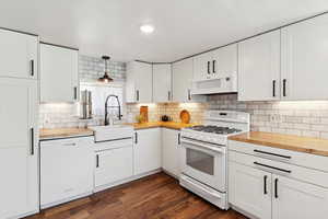 Kitchen featuring white appliances, butcher block countertops, decorative backsplash, and white cabinets