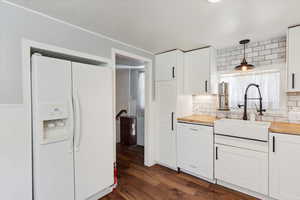Kitchen featuring white appliances, butcher block counters, backsplash, white cabinets, and pendant lighting