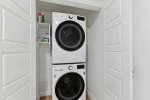 Washroom with stacked washer / drying machine and light wood-style flooring