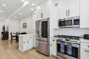 Kitchen featuring stainless steel appliances, recessed lighting, a peninsula, light countertops, and white cabinetry
