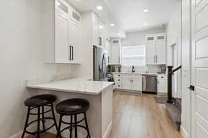 Kitchen featuring appliances with stainless steel finishes, a breakfast bar, a peninsula, white cabinets, and recessed lighting