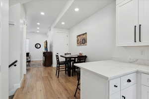 Kitchen with light wood-type flooring, recessed lighting, white cabinets, light stone counters, and a kitchen breakfast bar