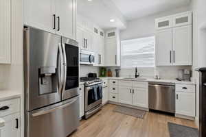 Kitchen with stainless steel appliances, white cabinetry, recessed lighting, glass insert cabinets, and light wood finished floors