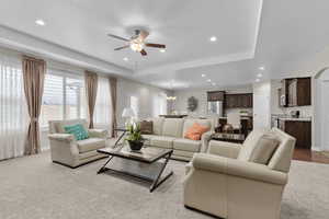 Living room featuring ceiling fan, recessed lighting, light colored carpet, a tray ceiling, and a chandelier