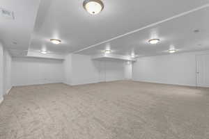 Finished basement with light colored carpet and a textured ceiling