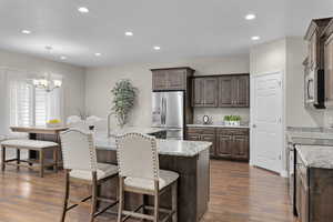 Kitchen featuring appliances with stainless steel finishes, dark wood-style flooring, dark brown cabinetry, recessed lighting, and a kitchen breakfast bar