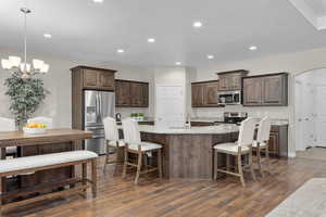 Kitchen with appliances with stainless steel finishes, dark brown cabinetry, dark wood-type flooring, arched walkways, and a breakfast bar area