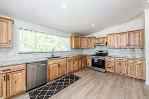 Kitchen featuring appliances with stainless steel finishes, under cabinet range hood, vaulted ceiling, crown molding, and decorative backsplash