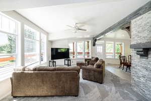 Carpeted living area with plenty of natural light, ceiling fan, a stone fireplace, and wood finished floors