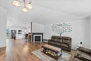 Living area with vaulted ceiling, wood finished floors, a tile fireplace, and a chandelier