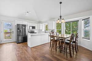 Kitchen featuring stainless steel appliances, white cabinetry, hardwood / wood-style floors, a chandelier, and vaulted ceiling