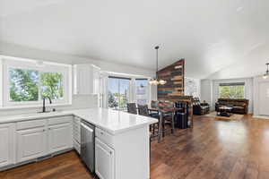 Kitchen featuring stainless steel dishwasher, a peninsula, dark wood-style flooring, vaulted ceiling, and open floor plan
