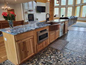 Kitchen featuring open floor plan, appliances with stainless steel finishes, a chandelier, a tile fireplace, and light stone counters