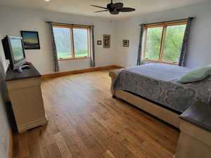 Bedroom with light wood finished floors, multiple windows, and ceiling fan