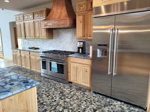 Kitchen with high end appliances, custom exhaust hood, tasteful backsplash, light brown cabinets, and recessed lighting
