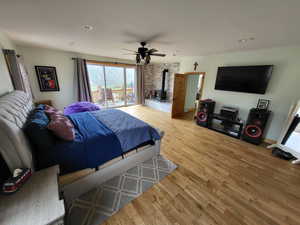 Bedroom featuring a wood stove, light wood finished floors, multiple windows, access to exterior, and recessed lighting