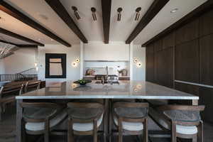 Kitchen with modern cabinets, beamed ceiling, a breakfast bar area, light stone countertops, and dark brown cabinetry