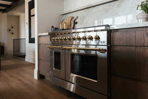 Kitchen view of range with two ovens, dark wood-style flooring, dark brown cabinetry, and tasteful backsplash