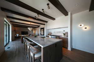 Kitchen featuring modern cabinets, beam ceiling, a large island with sink, a kitchen bar, and dark wood-style floors