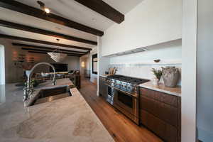 Kitchen with range with two ovens, beam ceiling, wood finished floors, custom range hood, and hanging light fixtures