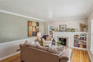 Living room featuring a fireplace, healthy amount of natural light, wood finished floors, and ornamental molding
