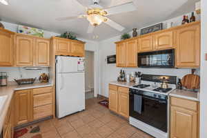 Kitchen with freestanding refrigerator, gas range, black microwave, a ceiling fan, and light tile patterned floors