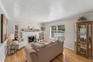 Living area with light wood finished floors, a tiled fireplace, a textured ceiling, and crown molding