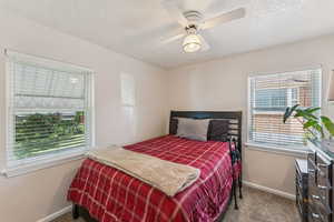 Carpeted bedroom featuring multiple windows, a textured ceiling, and ceiling fan