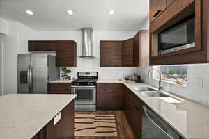 Kitchen with stainless steel appliances, wall chimney range hood, dark wood-style floors, decorative backsplash, and light stone counters