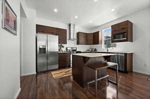 Kitchen with appliances with stainless steel finishes, wall chimney exhaust hood, modern cabinets, a breakfast bar area, and decorative backsplash