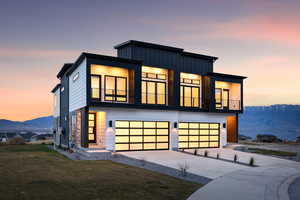 Contemporary home with an attached garage, a balcony, a lawn, board and batten siding, and concrete driveway