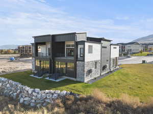 Rear view of property featuring a balcony, a mountain view, a yard, stone siding, and a patio