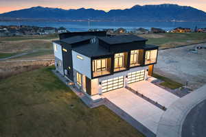 Rear view of house featuring a shingled roof, a garage, a balcony, concrete driveway, and a yard