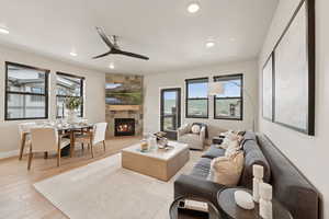 Living room with healthy amount of natural light, a tiled fireplace, a ceiling fan, light wood finished floors, and recessed lighting