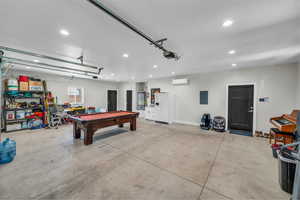 Garage featuring electric panel, recessed lighting, white refrigerator with ice dispenser, and a wall mounted air conditioner