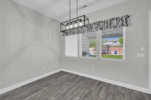 Unfurnished dining area with a chandelier and dark wood-style flooring