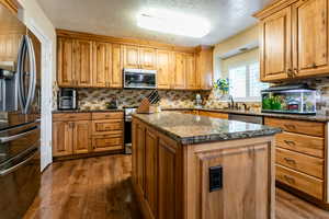 Kitchen with stainless steel appliances, dark wood-type flooring, backsplash, dark stone counters, and a textured ceiling
